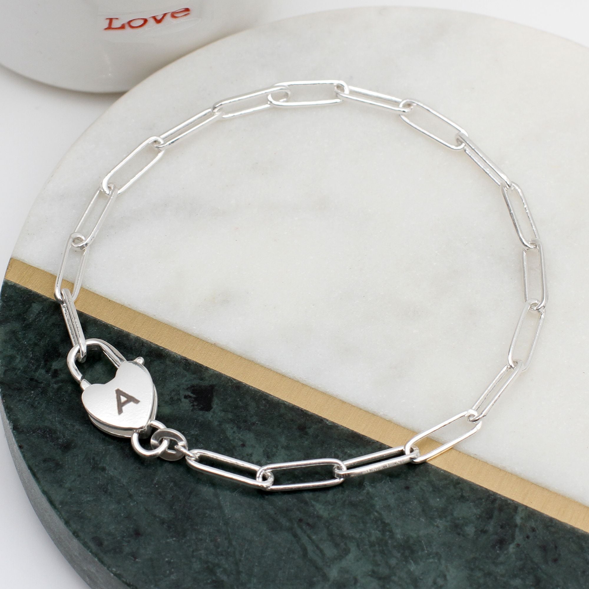 Silver chain bracelet with a heart padlock clasp engraved with the letter ‘A’.