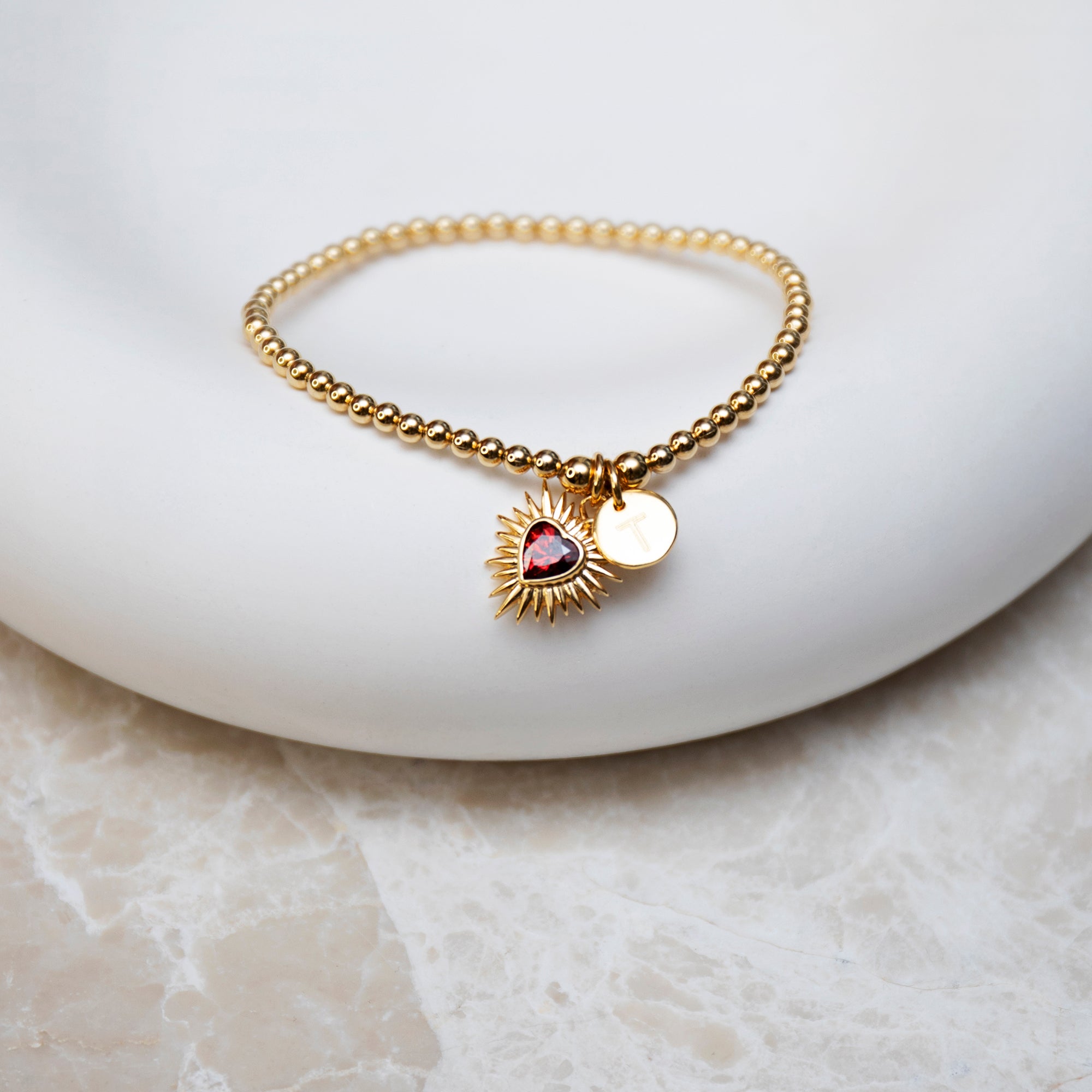Gold bracelet with a heart-shaped charm on a white dish