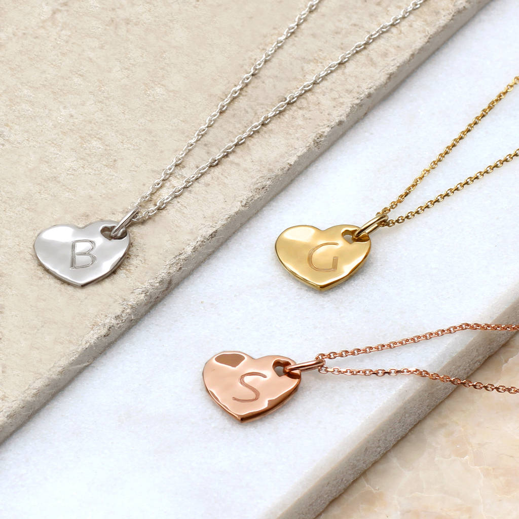 Three personalised heart pendant necklaces laid on a stone slab.