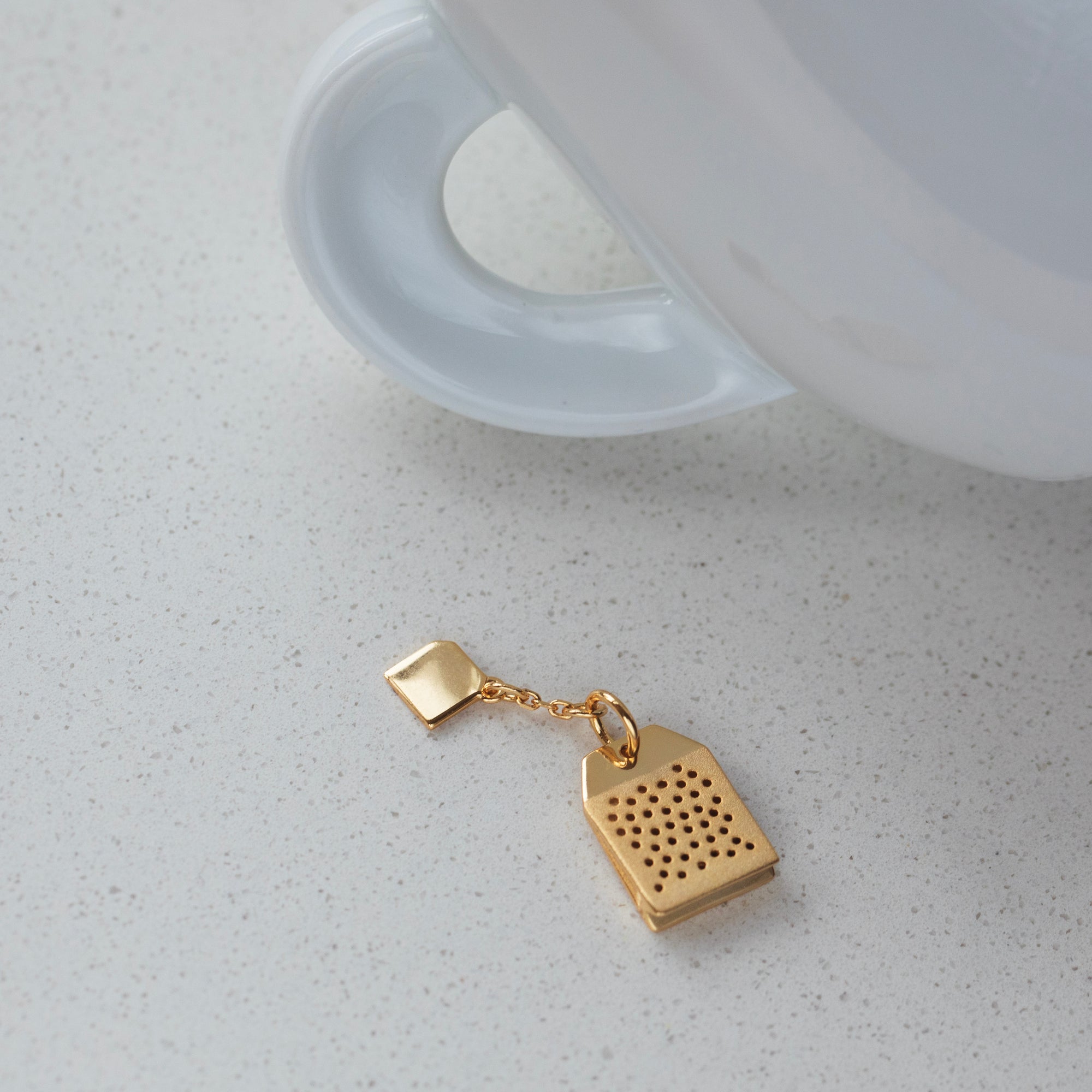 Gold tea infuser with a white teacup on a light gray surface