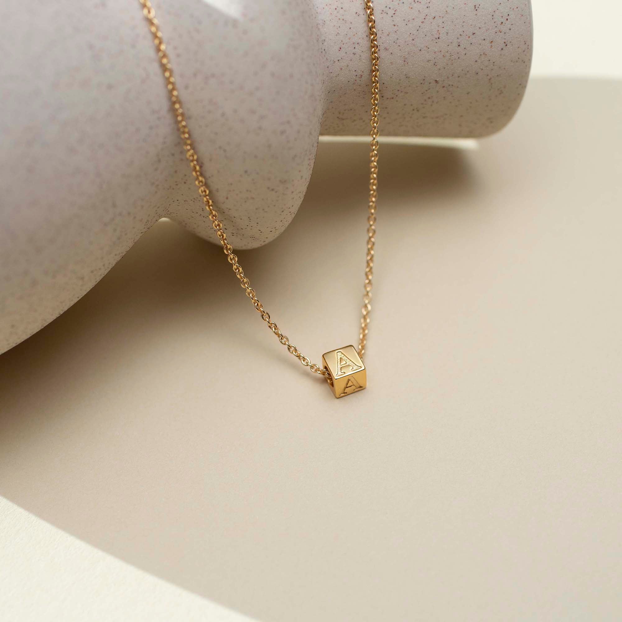Gold necklace with a square pendant on a neutral background