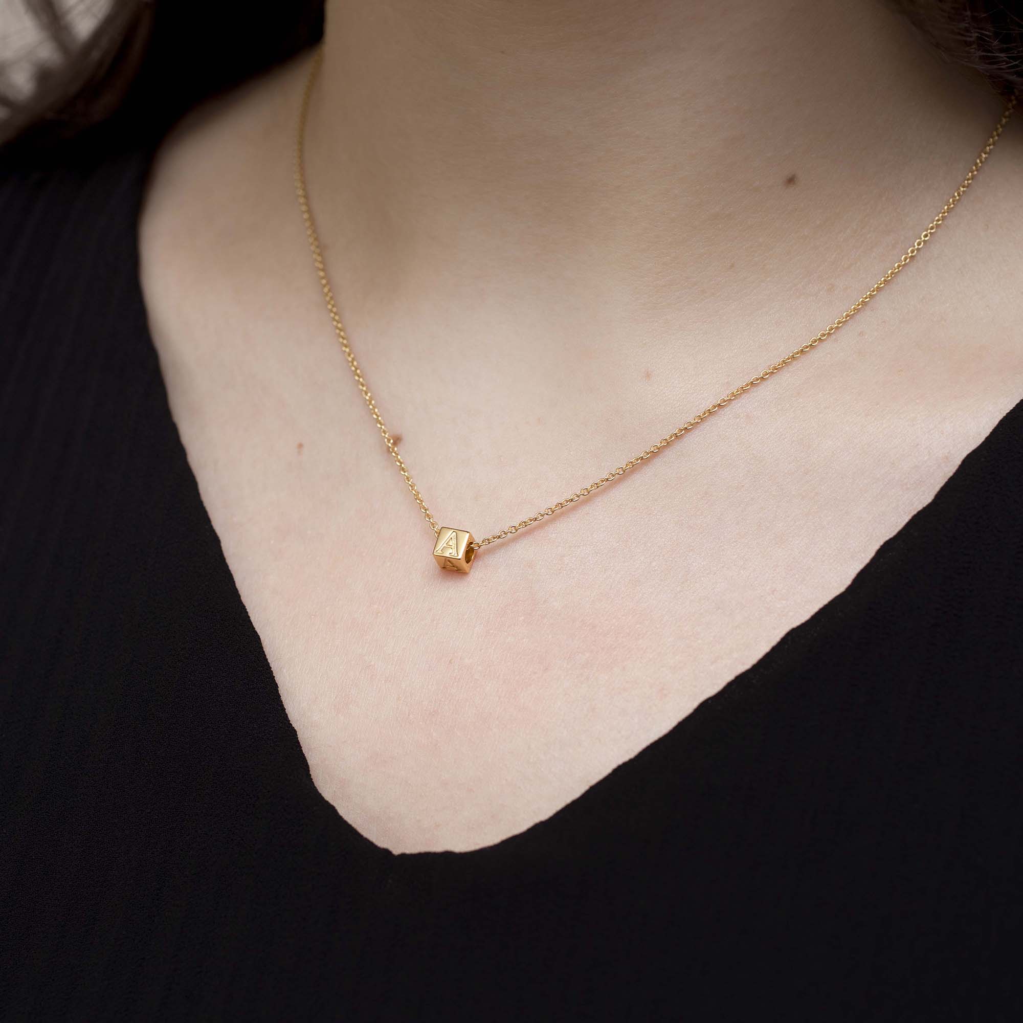 Gold necklace with a small pendant on a person wearing a black top.
