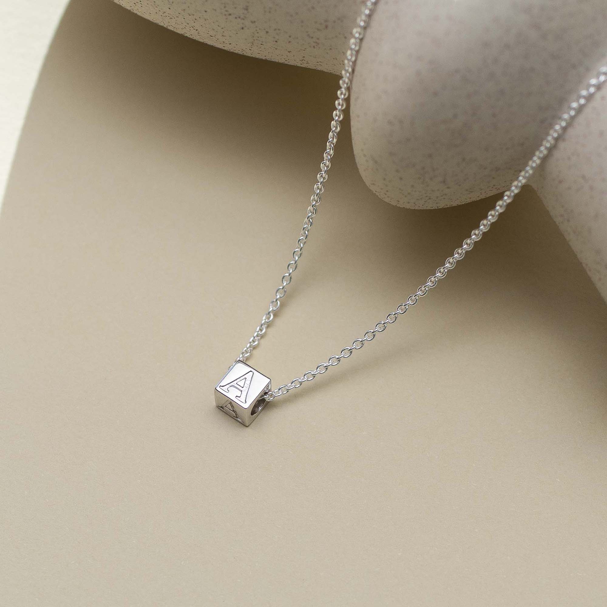 Silver necklace with a square pendant on a beige surface