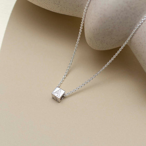 Silver necklace with a square pendant on a beige surface
