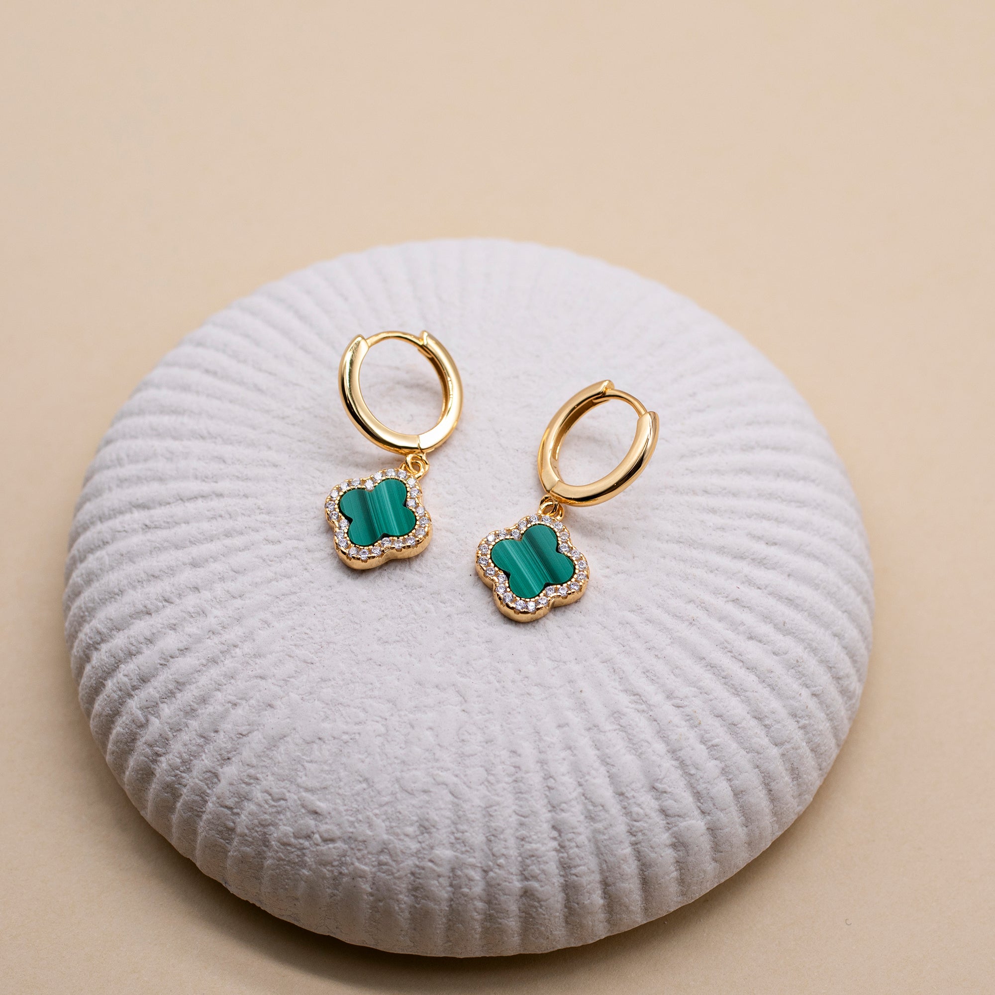 Gold earrings with green stones on a white cushion