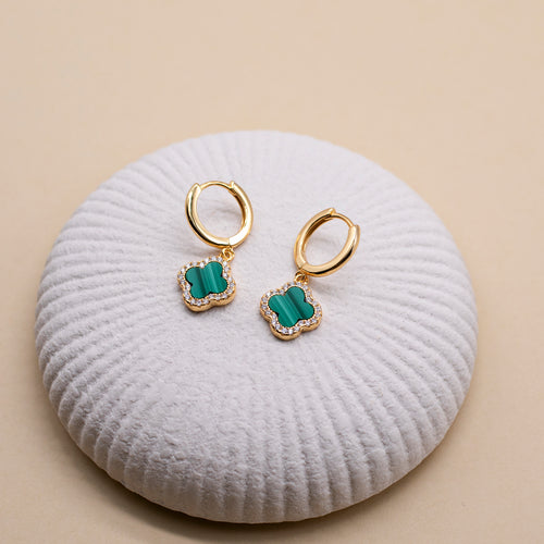 Gold earrings with green stones on a white cushion