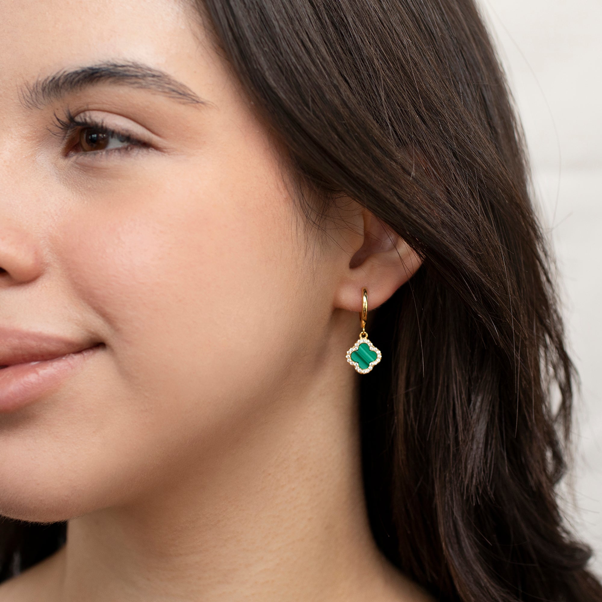 Close-up of a woman wearing gold earrings with green gemstones.