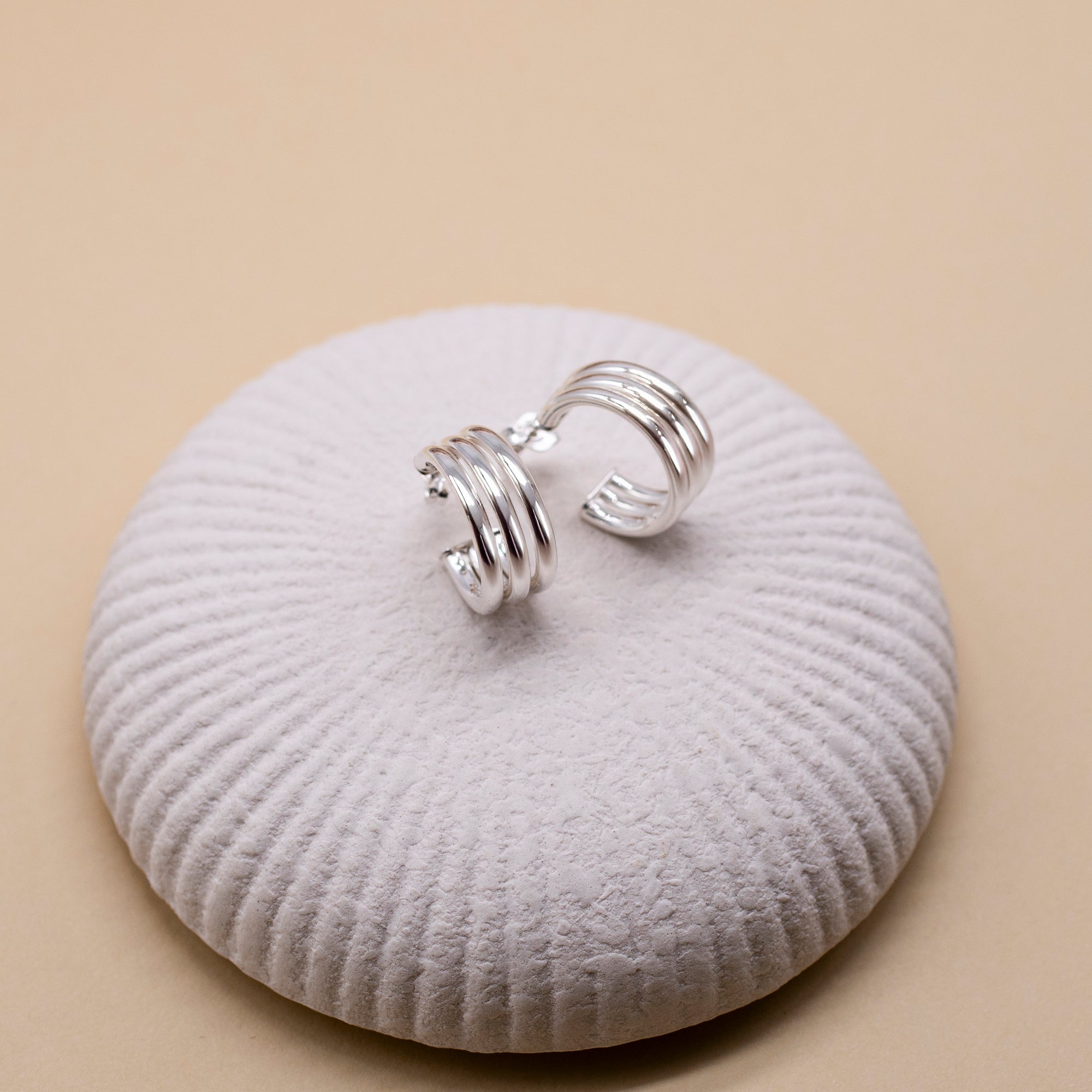 Silver spiral earrings on a gray cushion with a beige background