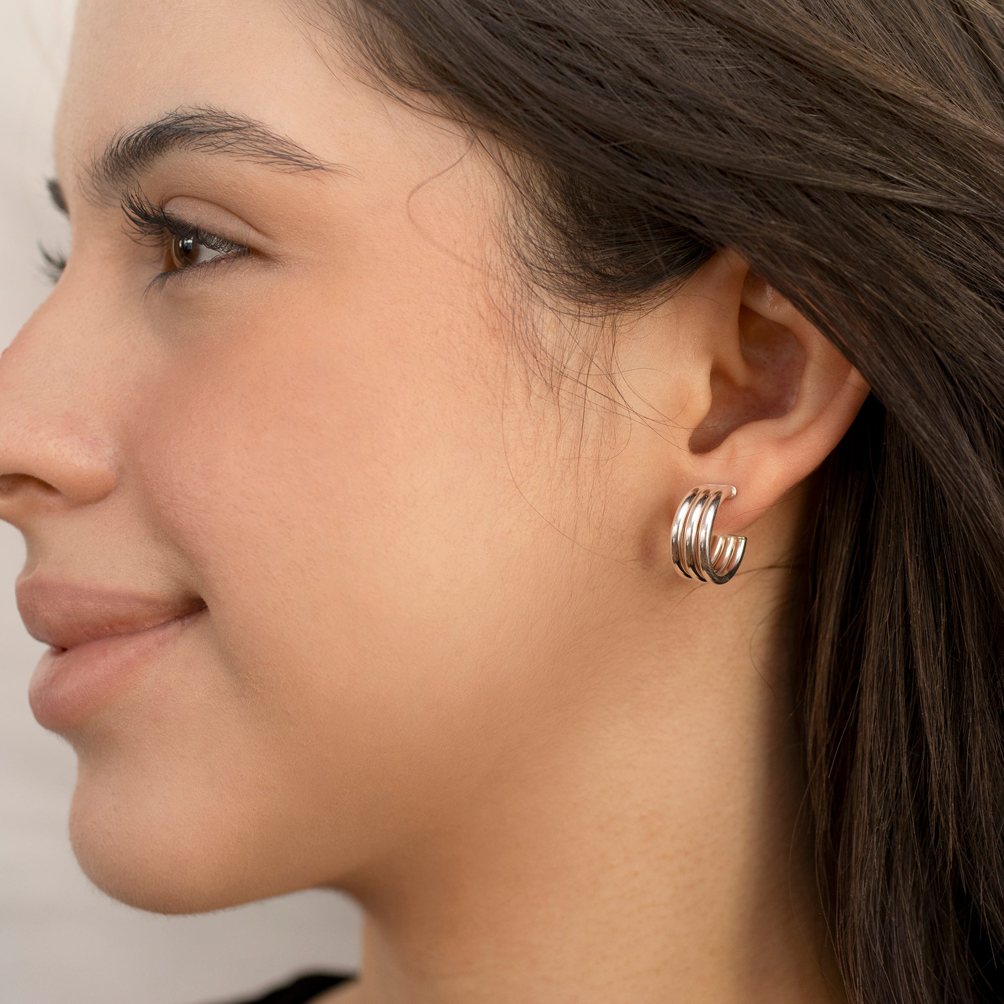 Close-up of a woman wearing gold hoop earrings with a neutral background