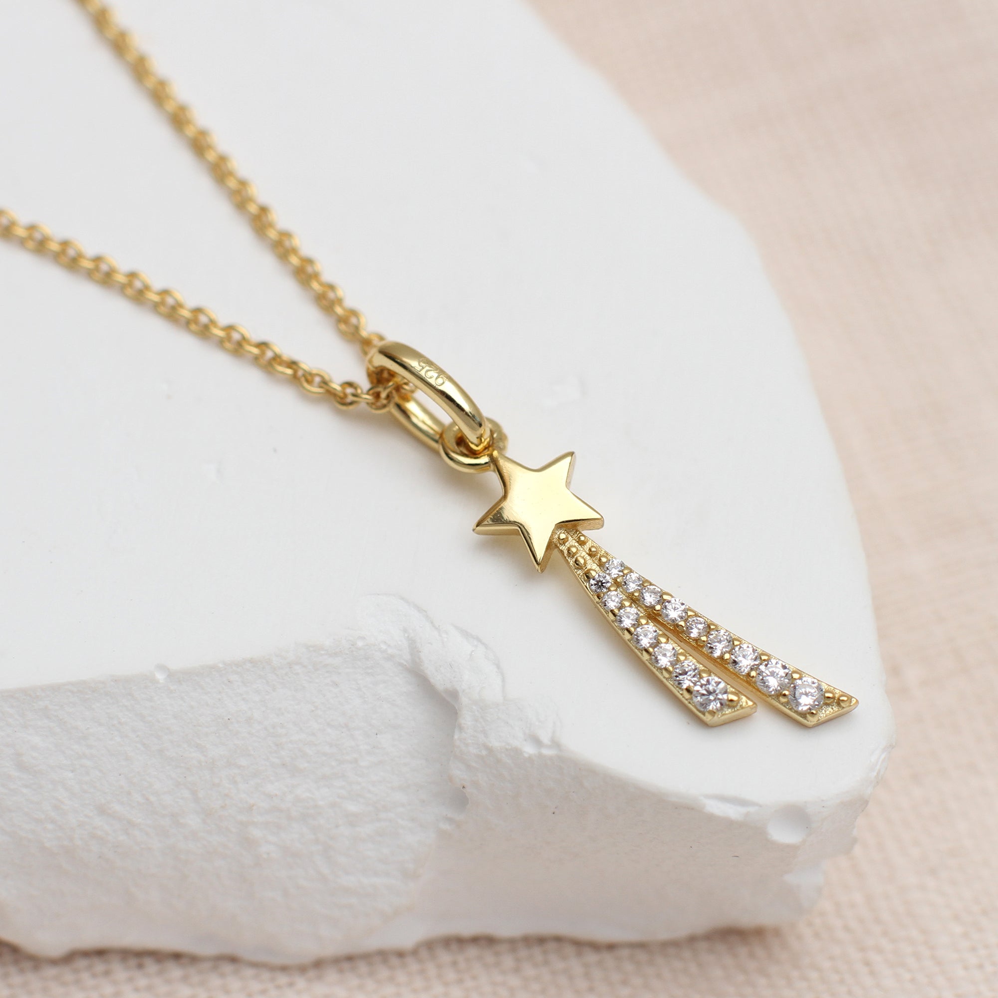 Gold necklace with star and diamond pendant on a white stone surface