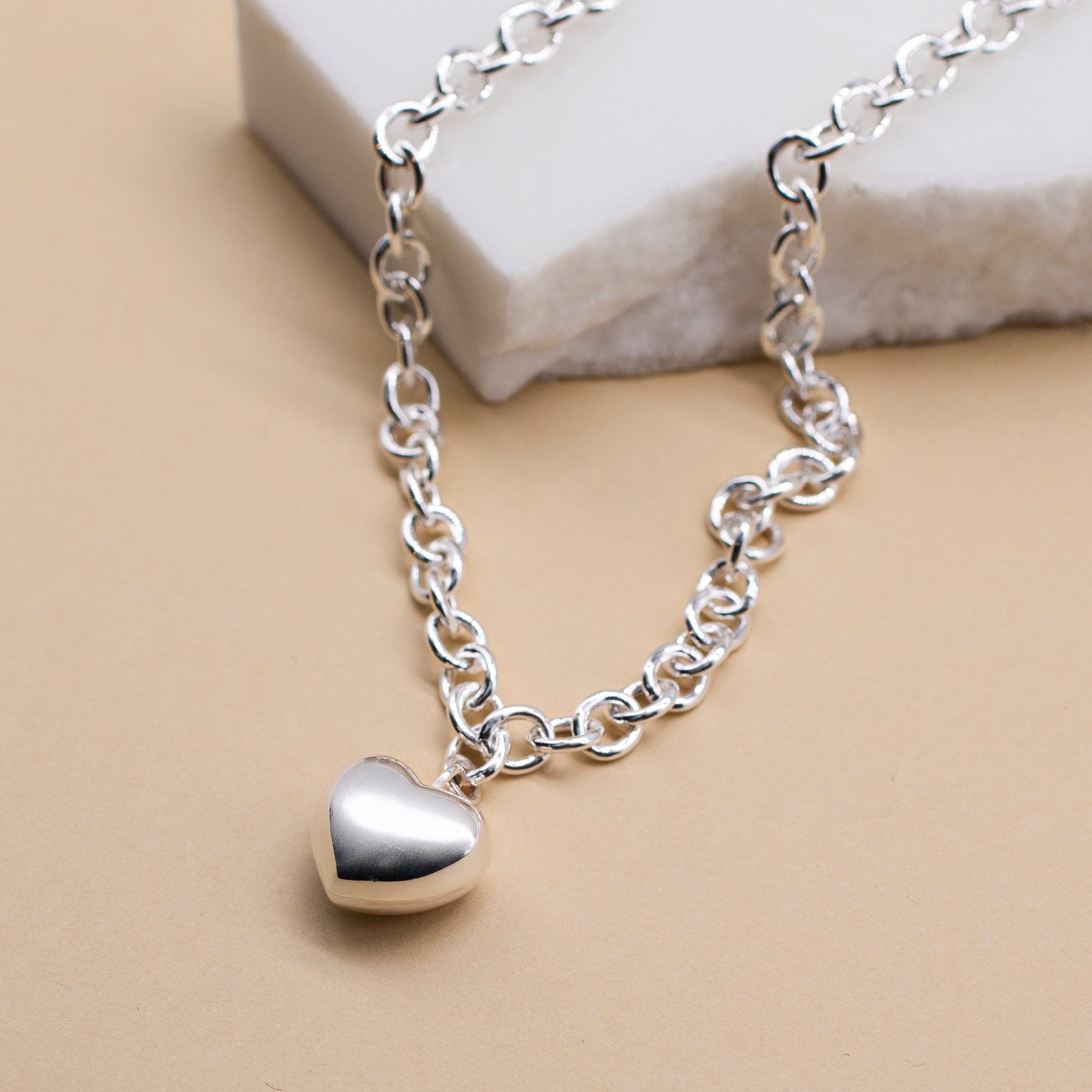 Silver heart-shaped pendant necklace on a beige background