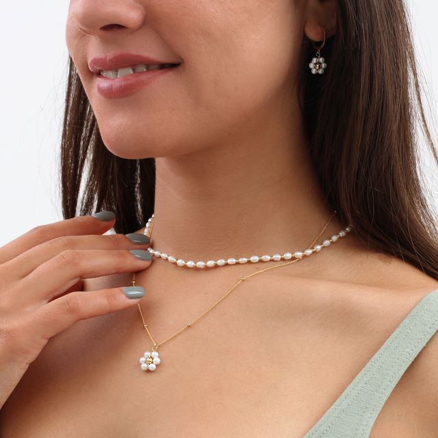 Woman wearing a stack of pearl necklaces, one freshwater pearl choker, and the other a gold chain with a pearl flower pendant.